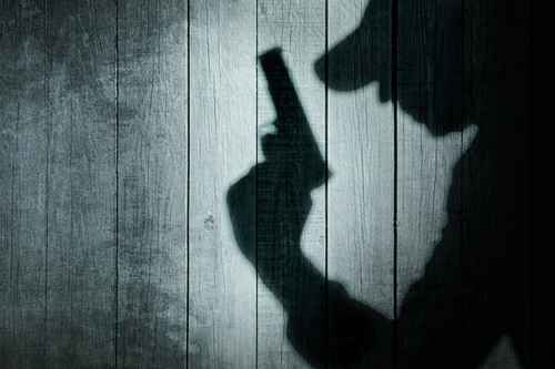 Man with a gun in shadow on a wooden background